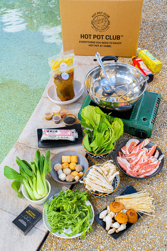 Hot Pot Club's Hot Pot Kit laid out by the swimming pool at home. Ingredients include thin-sliced meat, Asian vegetables, 2 organic broths (Clear vegan and Chicken Laksa), mixed fishablls, mixed mushrooms, and equipment.
